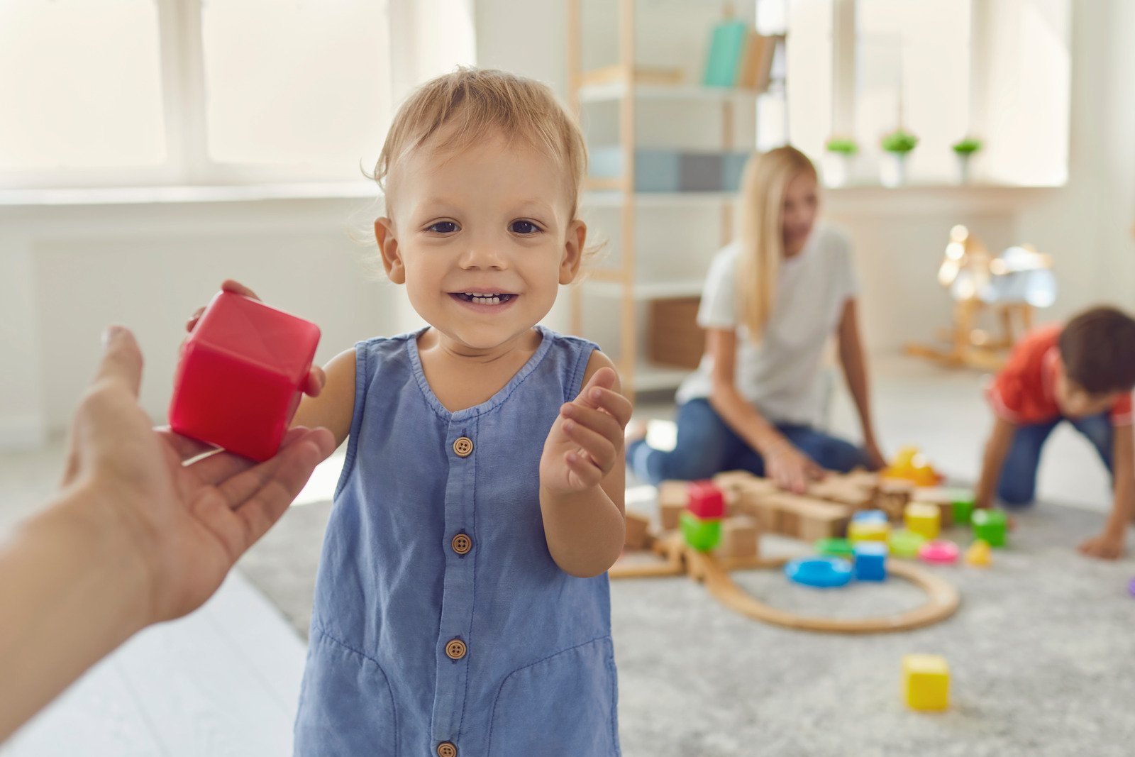 Happy Little Boy Gives a Red Plastic Cube in the Hands of His Dad in a Bright Room.