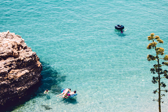 Man and Woman Swimming in the Sea Near Brown Cliff