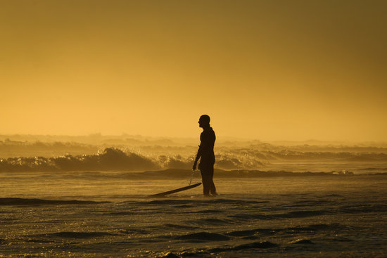 Man Standing on Seashore While Holding His Surfing Board during Sunset