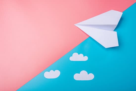 White Paper Origami Airplane With Clouds Lies On Pastel Blue